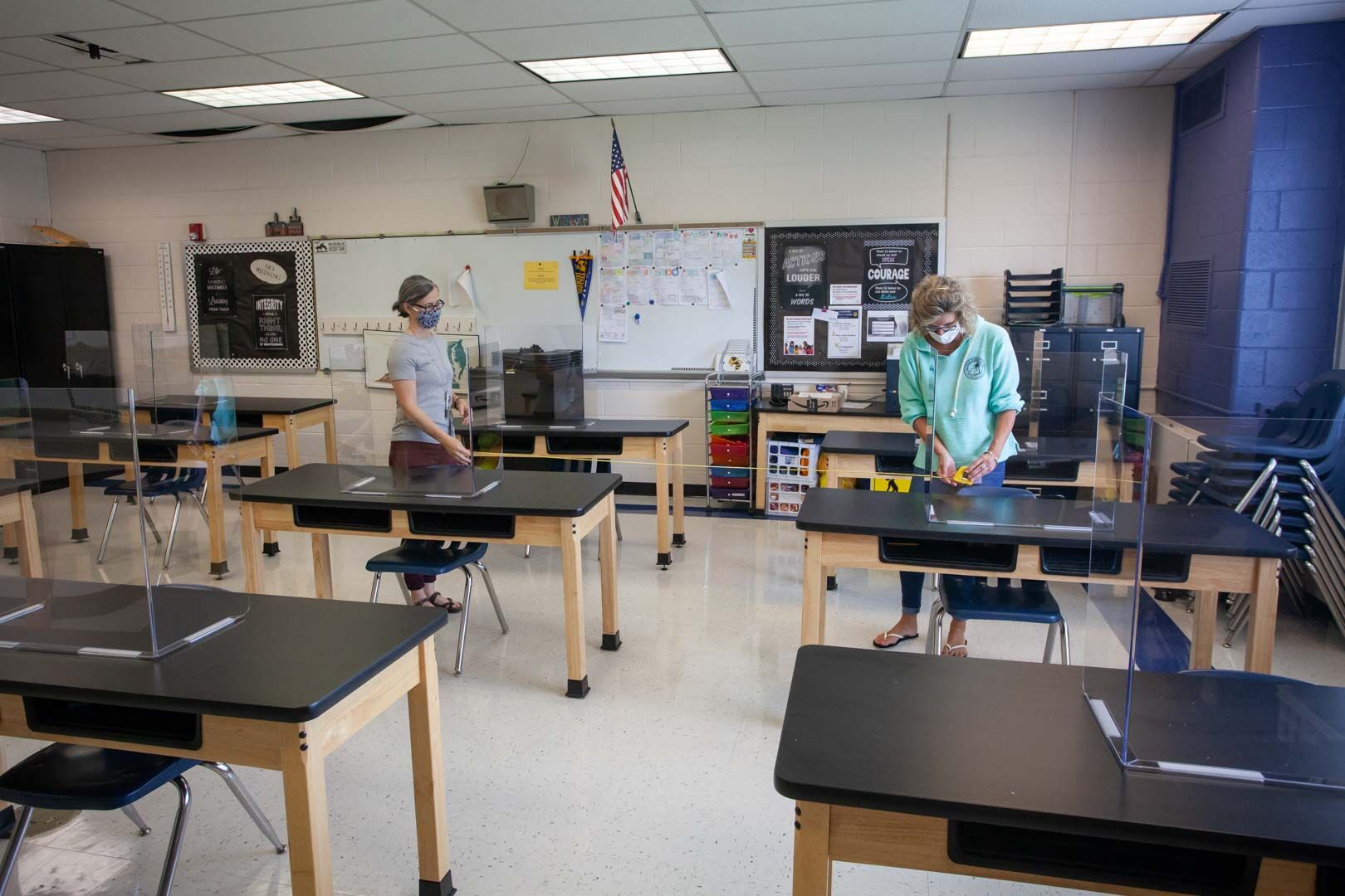Elementary teachers Elaine McCabe and Julie Ruth measure desks with clear plexiglass barriers installed atop.