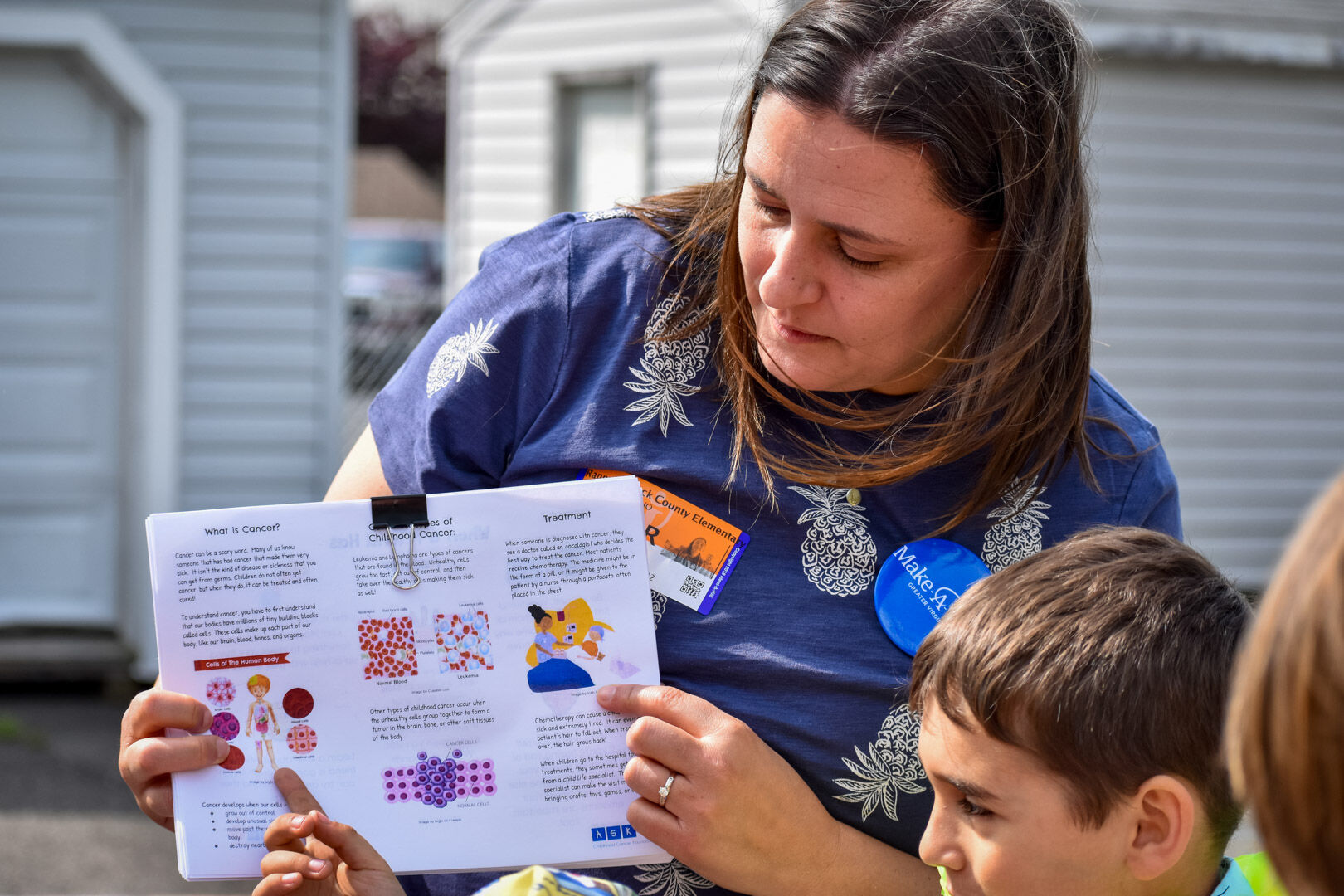 Lynnie Genho, Anne’s mom, shares an informative handout from the ASK Childhood Cancer Foundation with Christopher Creel and other 3rd grade students.