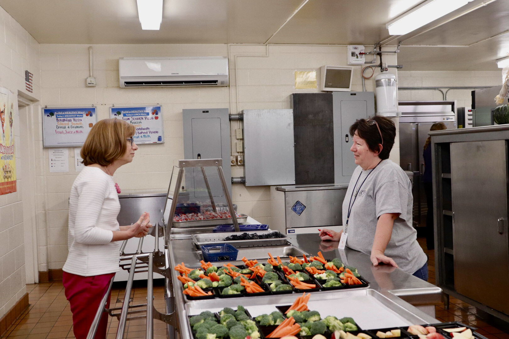 Cindy Long, administrator of the Food and Nutritional Services agency, thanks lunchroom staff member Wanda Early for her part in serving students healthy and nutritious lunches. After touring the courtyard, Long put on an apron and gloves and helped serve lunch to third graders.