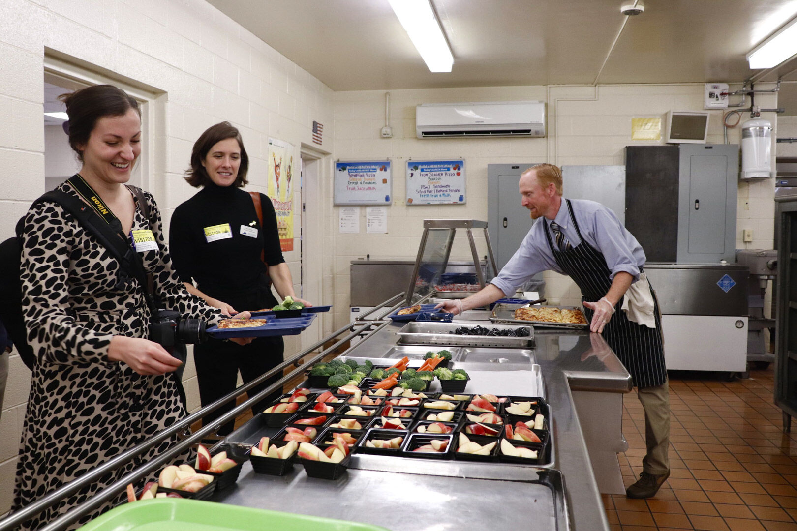 Representatives from the Virginia Department of Education grab a lunch tray at the Rappahannock County Elementary School cafeteria. After all of the third grade students were served lunch, guests had an opportunity to try scratch-made pizza and locally grown apples. Farmer and chef Brian Volmrich (right) was hired using funds from a federal grant and has started serving several new scratch-made recipes in Rappahannock school cafeterias.