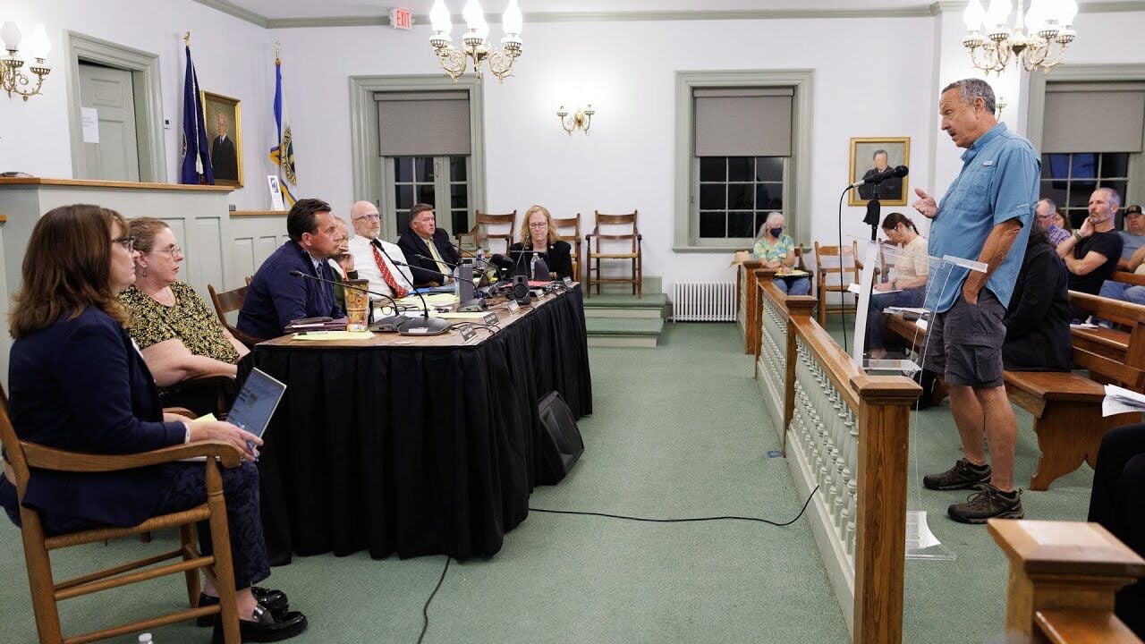 a man stands at a podium in front of the Board of Supervisors in the courtroom.