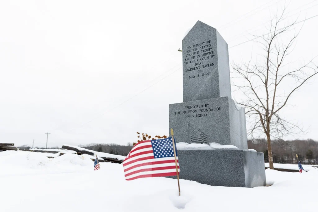 a picture of a monument at Madden's tavern covered in snow with a small american flag in front of it