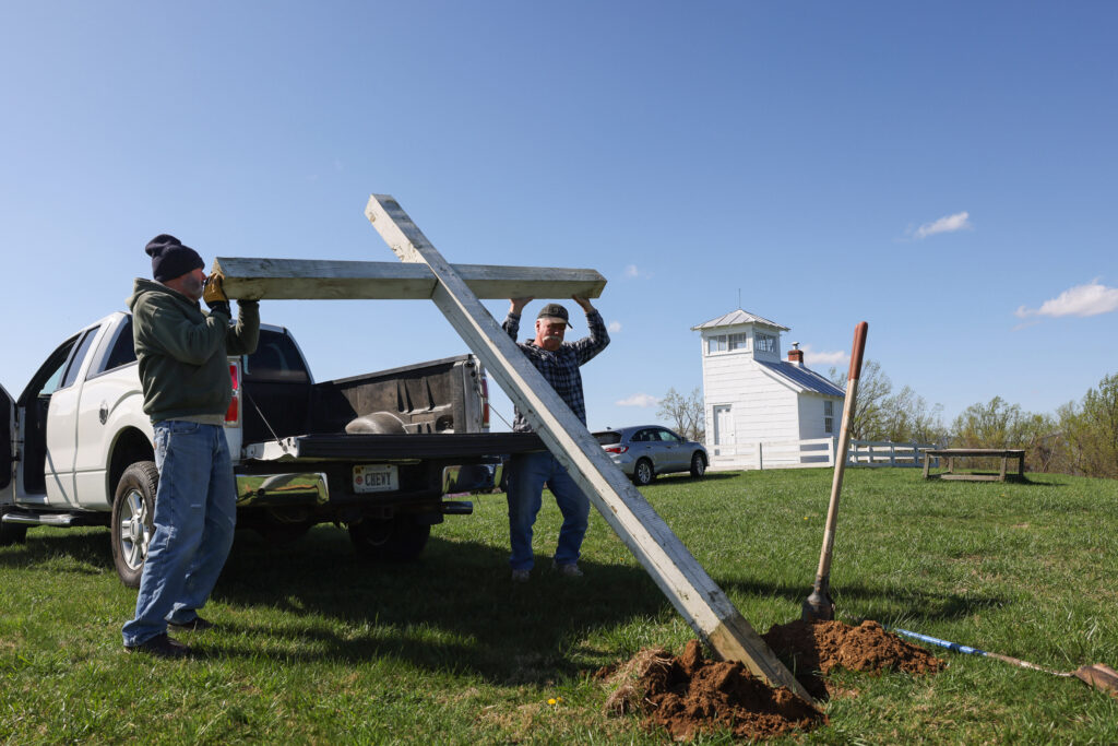 two men lift a large wooden cross out of the flatbed of a pickup truck
