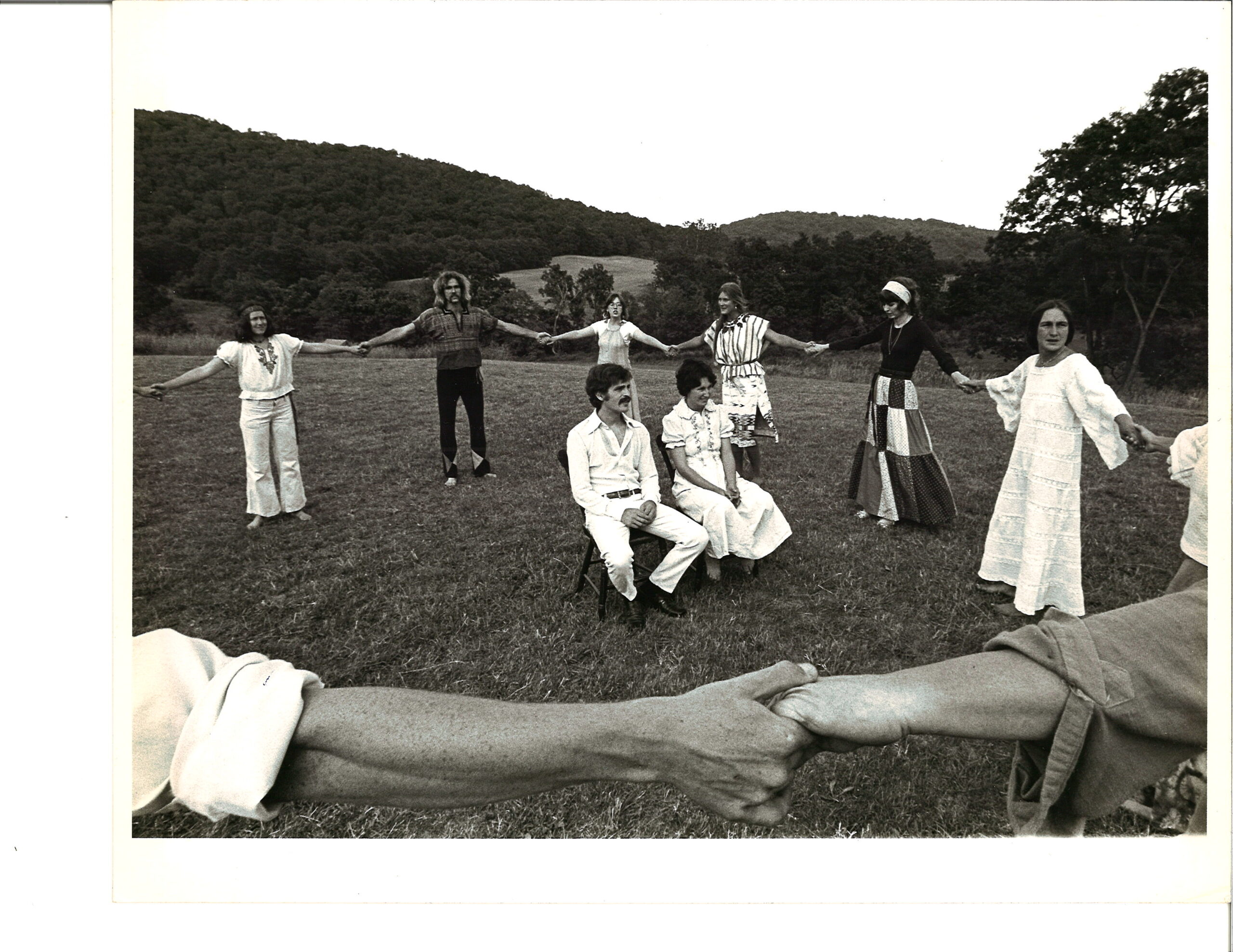 people holding hands in a circle dancing around a newly married couple in chairs in a field